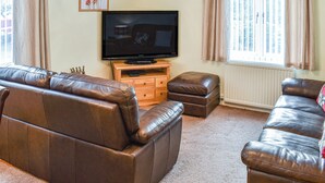A living room with a brown leather sofa, a television on a wooden stand, and a window with curtains. - 2 bedroom accommodation in Ambleside (Ambleside)
