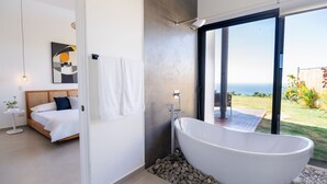 A modern bathroom with a freestanding bathtub, a large window, and a view of the ocean. - Oceanvista Villa I Santa Teresa Beach  Brand New Oceanview Villa Gated Community (santa teresa)