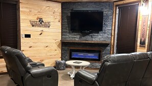 Un interior acogedor con pared de piedra, televisor de pantalla plana, sillones de cuero y chimenea.