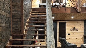 Una escalera de madera con diseño rústico, un sillón de cuero reclinable y un cartel de bienvenida en un interior moderno.