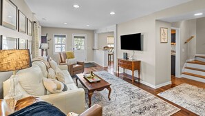 A spacious living room with a sofa, coffee table, and a TV. There is a staircase leading to another level. - Sunshine Manor (New Bern)