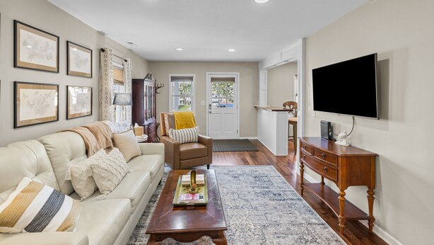 A living room with a sofa, armchair, coffee table, TV, and framed pictures on the wall. - Sunshine Manor (New Bern)