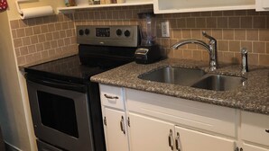 Una cocina con armarios blancos, un fregadero de acero inoxidable y una estufa negra.