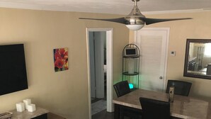 Una sala de estar con un sofá, una mesa de comedor con sillas, un televisor y un ventilador de techo.