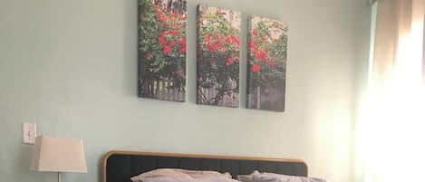 A bedroom with a bed, a nightstand, a lamp, and three wall-mounted paintings.