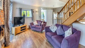 A modern living room with a TV, two purple sofas, wooden flooring, and a staircase. - Ty Teiliwr - UK45719 (Tyn Y Gongl, near Benllech)