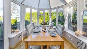 A conservatory with a wooden table set for dining, large windows, and a view of greenery outside. - Ty Teiliwr - UK45719 (Tyn Y Gongl, near Benllech)