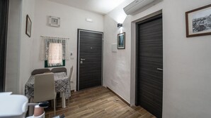 Een smalle gang met een eettafel en stoelen, twee donkere deuren en een airconditioning aan de muur.