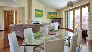 A spacious living area with a glass dining table, a sofa, and a fireplace. There are two paintings on the wall and a television on a stand. - Villa Paradiso–Villa with private pool, Umbria (Trestina)