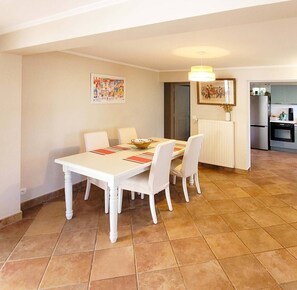 Un comedor con una mesa y sillas blancas, una cocina al fondo y un radiador en la pared.