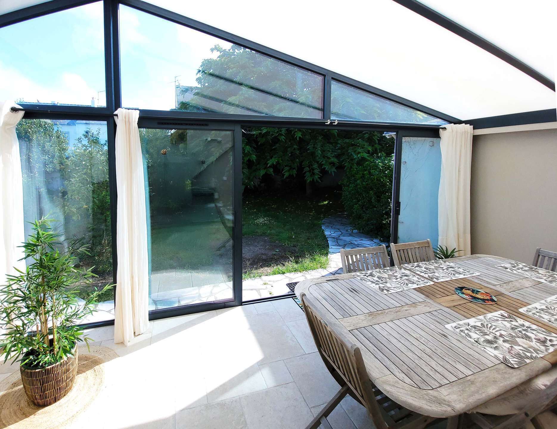 A conservatory with a table and chairs, large glass doors, and a potted plant.