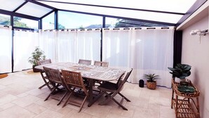 A covered patio with a table and chairs, potted plants, and a view through the glass roof.