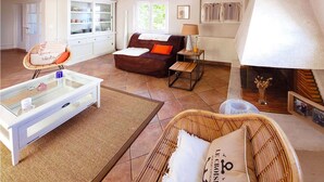 A living room with a sofa, a glass coffee table, a wicker chair, a fireplace, and a cabinet with glass doors.