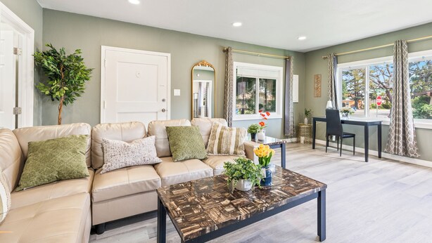 Un salon avec un canapé beige, une table basse et une vue sur l’extérieur grâce à de grandes fenêtres.
