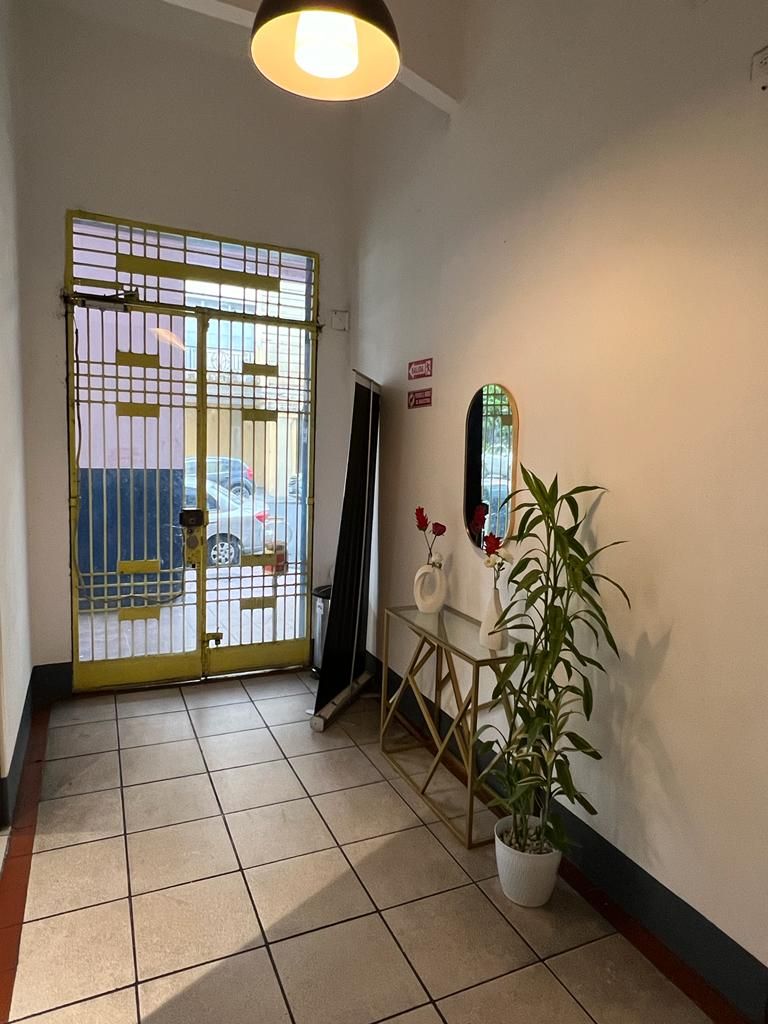 A hallway with a tiled floor, a yellow door with a metal gate, a potted plant, a mirror, and a sign on the wall.