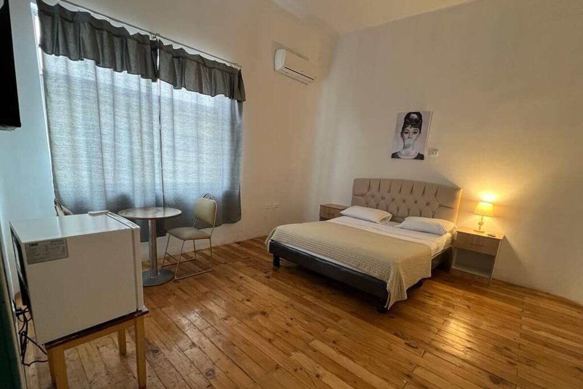 A bedroom with a bed, bedside table, lamp, and a small desk with a chair.