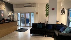 A reception area with a wooden counter, black sofas with blue cushions, a large plant, and a glass door leading outside. - HOTEL PERLA CENTRAL MALECON (Guayaquil)