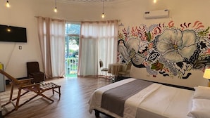 A hotel room with a bed, a wooden chair, a small table, and a large floral mural on the wall. - HOTEL PERLA CENTRAL MALECON (Guayaquil)