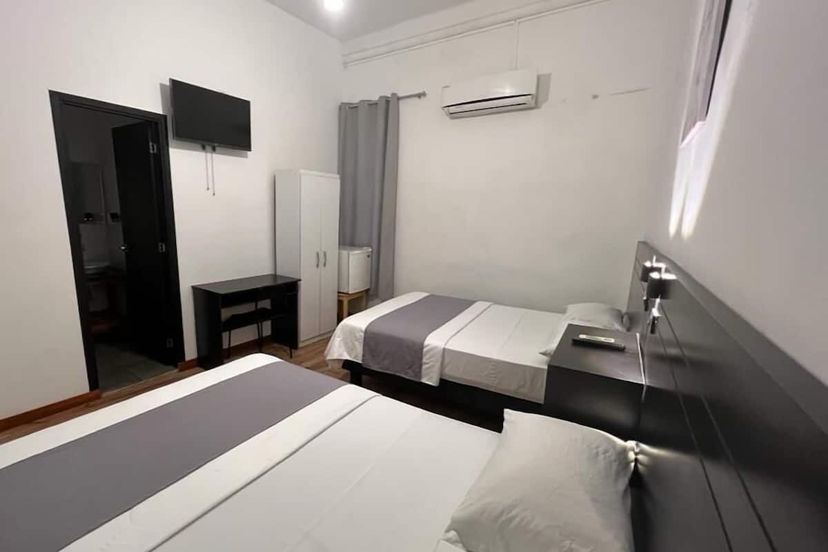 A bedroom with two beds, a desk, a wardrobe, and an air conditioning unit.