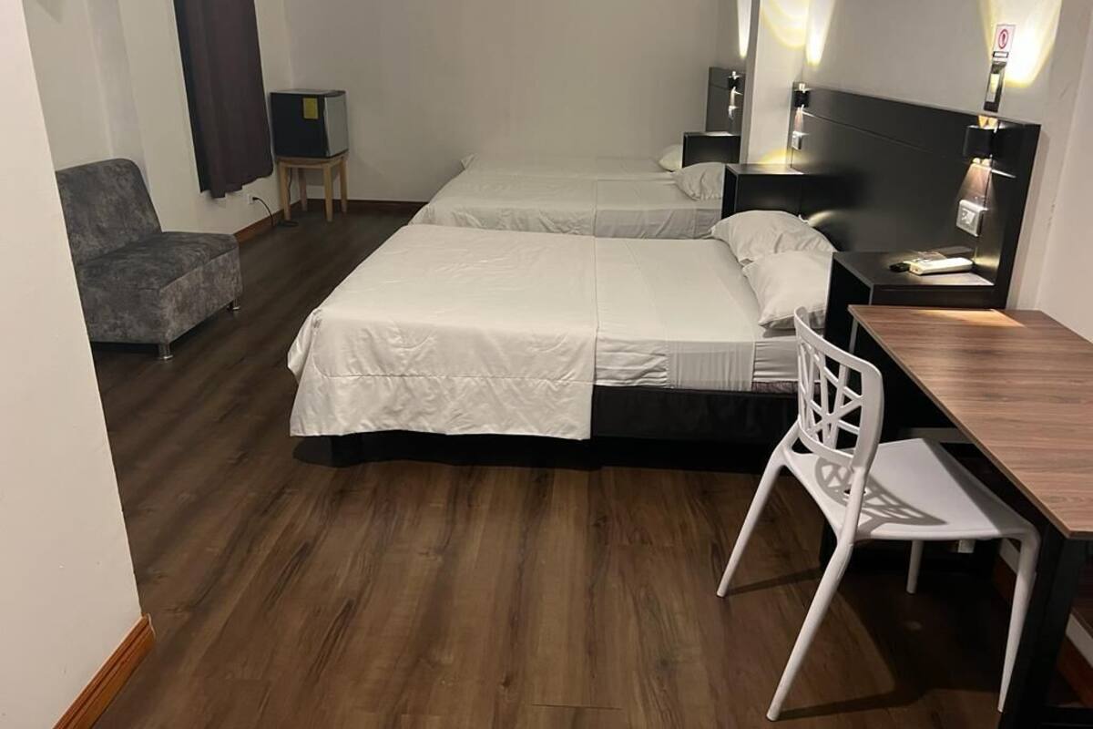 A hotel room with two beds, a desk, a chair, a TV, and a small table.