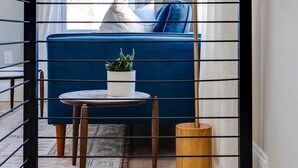 Un escalier, un canapé bleu, une petite table ronde avec une plante et un grand lampadaire.