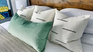 Un lit avec des oreillers blancs et un oreiller vert, une tête de lit en bois et une lampe.