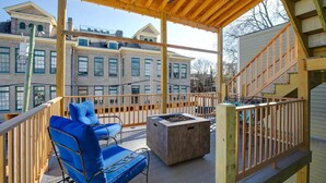 Un espace extérieur abrité doté d’une terrasse en bois, d’un fauteuil bleu rembourré, d’un petit foyer et d’un escalier menant à un niveau supérieur.