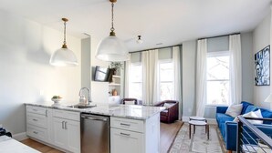 Une cuisine moderne avec des meubles blancs, un lave-vaisselle encastré et des luminaires suspendus.