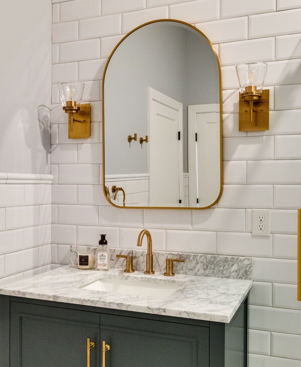 A bathroom with a white tiled wall, a gold-framed mirror, a marble countertop, and a dark-colored cabinet. - Gorgeous new home in Churchill
(Richmond)