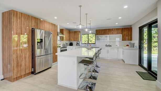 Una cocina moderna con una isla central, electrodomésticos de acero inoxidable, paneles de madera y un ventanal grande.