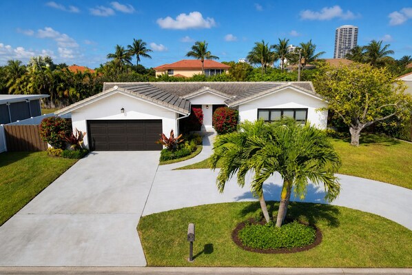 A modern two-story house with a garage, a driveway, and a well-maintained lawn with palm trees. - Beach House with Pool, Luxurious & Contemporary (West Palm Beach)
