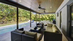 Un espacio al aire libre cubierto con mobiliario de mimbre, piscina y vistas a un jardín exuberante.