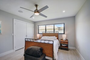 A bedroom with a bed, a ceiling fan, a window, a nightstand, and a chair. - Beach House with Pool, Luxurious & Contemporary (West Palm Beach)