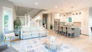 A spacious living area with a sofa, a coffee table, and a kitchen with a central island and bar stools. - Tranquil Shores | Lake Michigan | Private Beach | Sleeps 11 (Norton Shores)