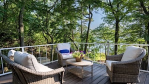 A deck with wicker furniture and a small table, surrounded by a white railing and lush greenery. - Tranquil Shores | Lake Michigan | Private Beach | Sleeps 11 (Norton Shores)