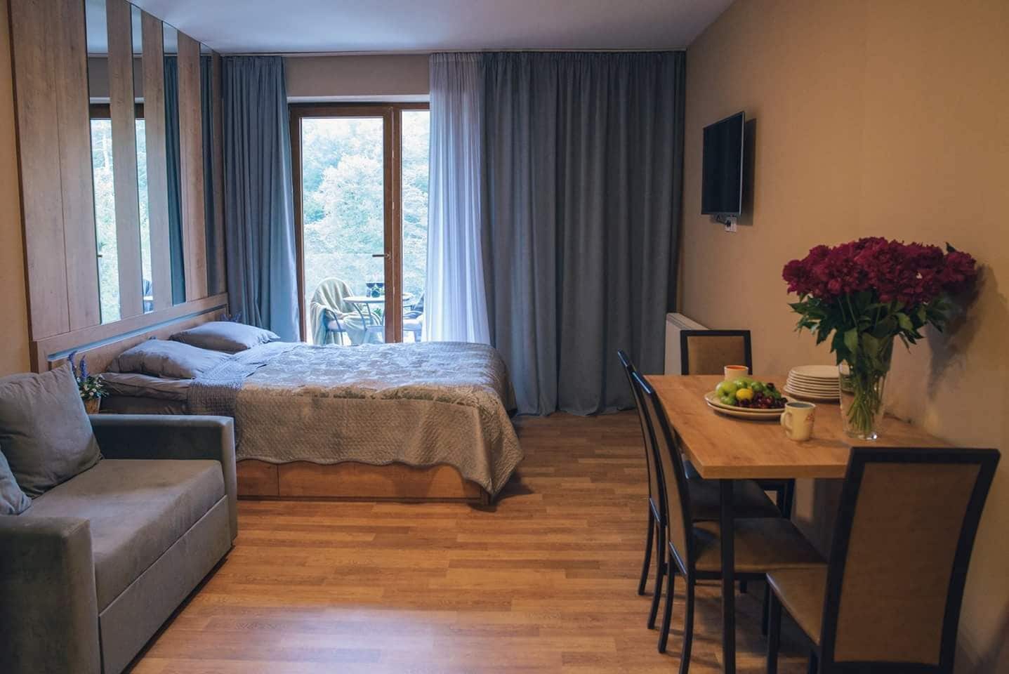 Une chambre à coucher comprenant un lit, un canapé, une table à manger avec des chaises, un téléviseur et une fenêtre avec des rideaux.