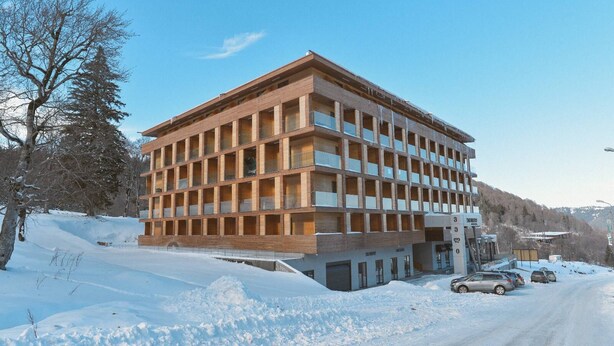 Un edificio a più piani con facciata a griglia, situato in una zona innevata sotto un cielo sereno.