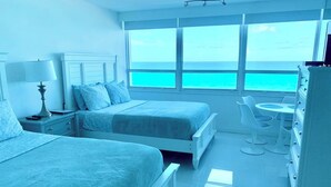 Quarto com duas camas, uma escrivaninha e vista para o oceano.