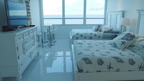 Ein Schlafzimmer mit großem Fenster, Fernseher, Schreibtisch und einem Bett mit Wellenmuster.