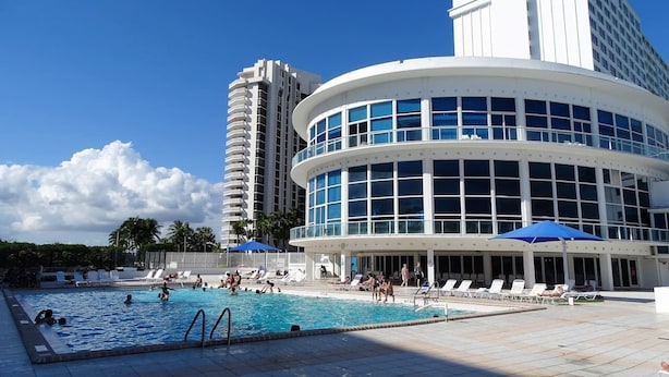 Et hotel med swimmingpool, liggestole og en høj bygning i baggrunden.