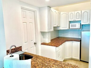 A kitchen with white cabinets, a granite countertop, a stainless steel sink, and a built-in microwave.