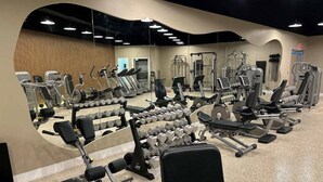 Et fitnesscenter med forskellig træningsudstyr, herunder løbebånd, styrkemaskiner og håndvægte.