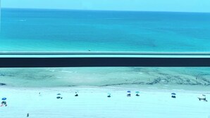 Blick auf einen Strand mit blauem Himmel, ruhiger See und mehreren Sonnenschirmen im Sand.