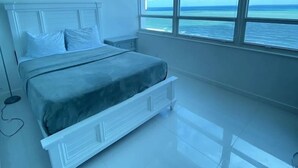 Een slaapkamer met een bed, een nachtkastje, een raam met uitzicht op zee en een plafondlamp.