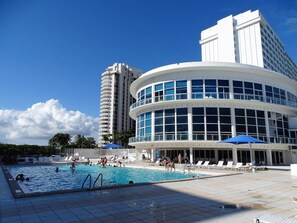A hotel with a swimming pool, lounge chairs, and a tall building in the background.
