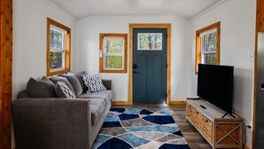 Una sala de estar acogedora con un sofá gris, un tapete azul y blanco, un televisor y un aparador de madera.