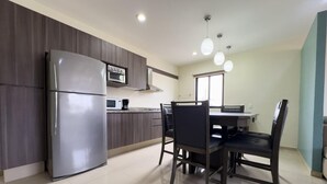 Una cocina moderna con refrigerador, microondas y estufa, una mesa de comedor con sillas e iluminación colgante.