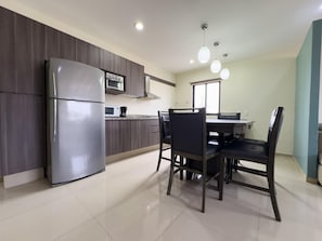 A modern kitchen with a refrigerator, microwave, and stove, a dining table with chairs, and pendant lighting.