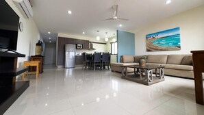 Una sala de estar moderna con un televisor de pantalla plana, un comedor con mesa y sillas, una cocina con refrigerador y estufa, y un ventilador de techo.