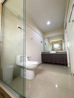 Une salle de bain avec une douche à parois de verre, des toilettes, un lavabo avec un miroir au-dessus et un sol carrelé.